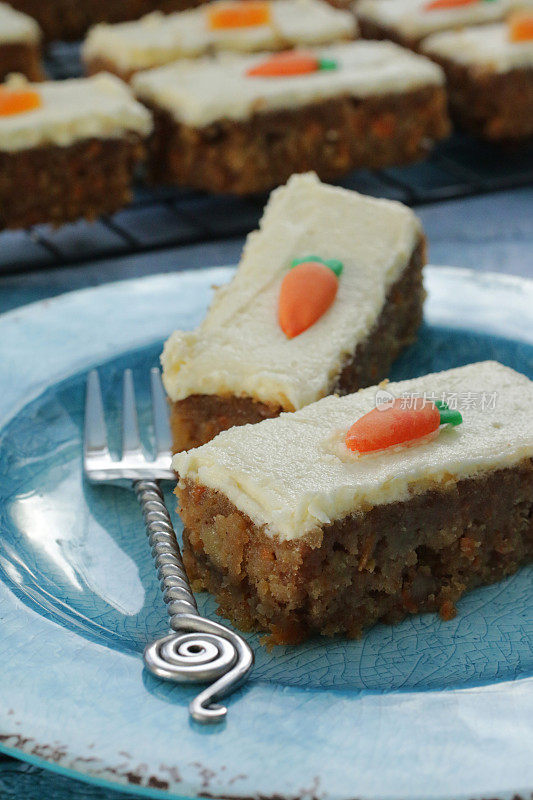 这是一个用叉子放在蓝色盘子上的自制胡萝卜蛋糕片，上面涂着香草味的奶油，果冻橙片和翻糖胡萝卜糖霜装饰的图片