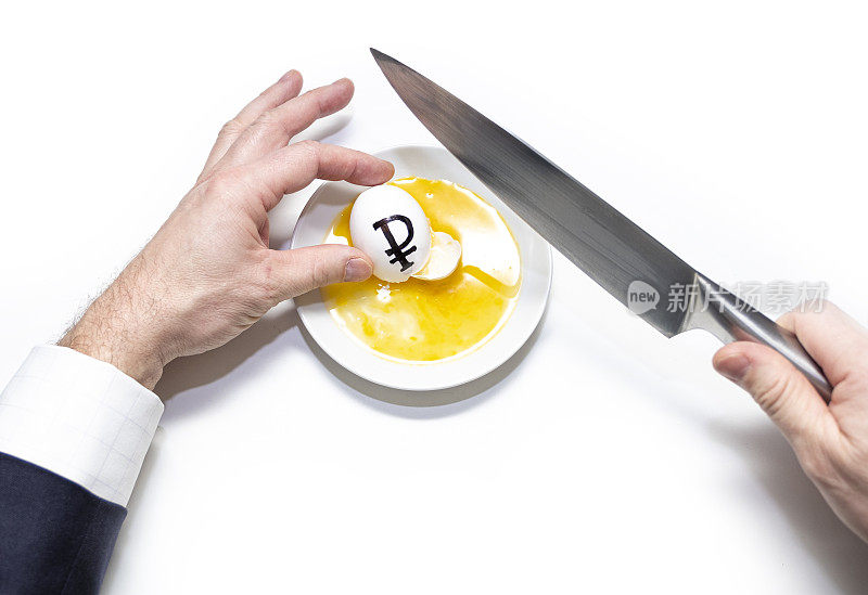 一名身穿西装的白人男子用刀打碎了一个带有俄罗斯卢布符号的鸡蛋。白色盘子里的蛋黄。
