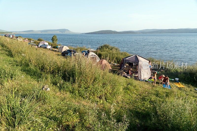 在一个阳光明媚的夏日，人们在大湖的岸边休息帐篷。
