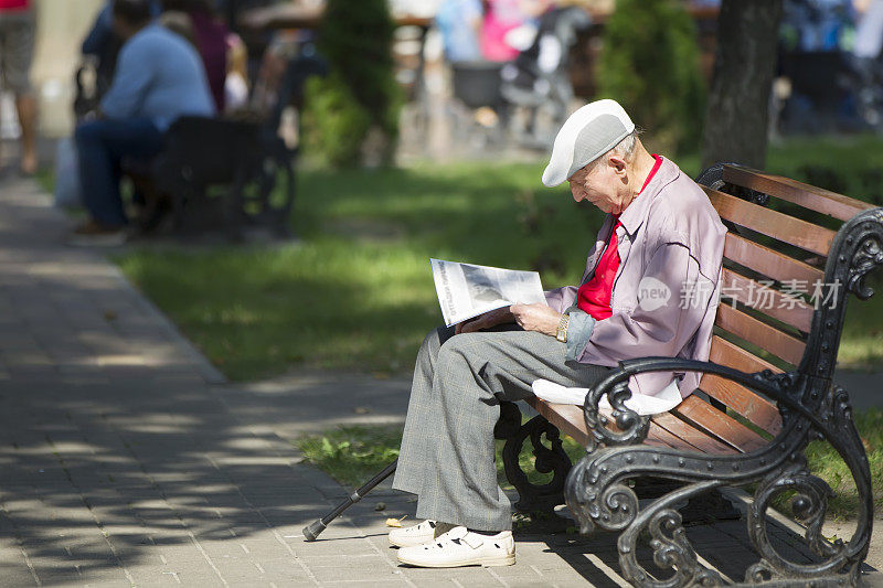 老爷爷坐在长凳上看报纸。那位老人躺在城市的街道上休息。年老的时候