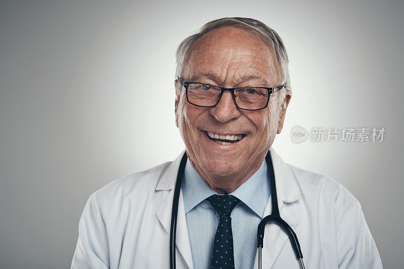 以灰色背景为背景拍摄的演播室里一位快乐的老年男医生
