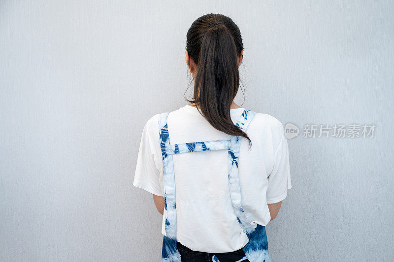 一个穿着蜡染围裙的女孩面对着墙，在一个干净舒适的环境中