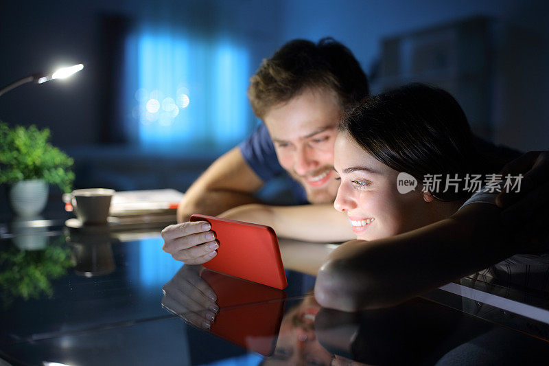 幸福的夫妇在晚上用智能手机看媒体