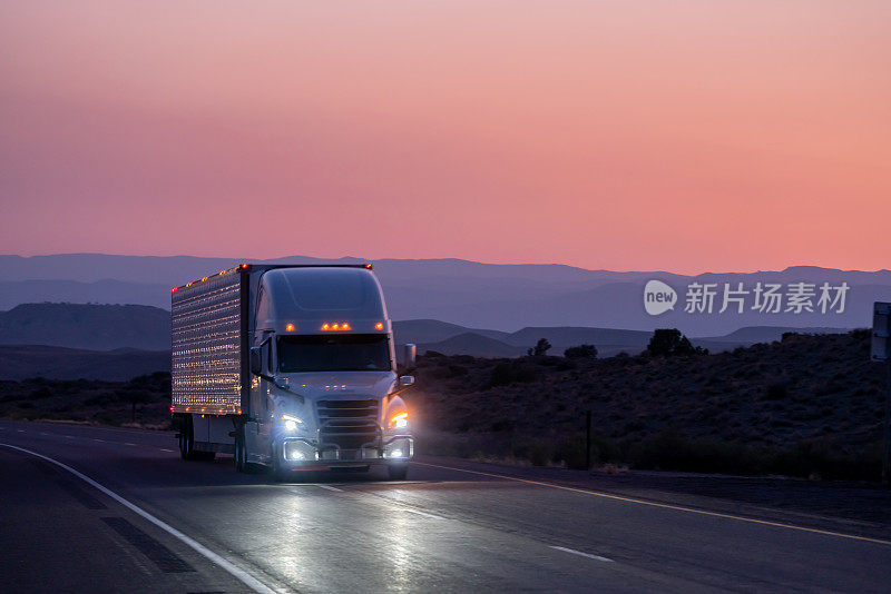 一辆往东行驶的半挂车在沙漠公路上运送货物，一个戏剧性的日落背景