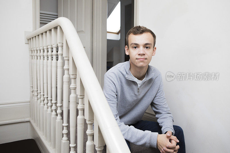 一名男大学生坐在一所房子的楼梯顶端看着摄像机