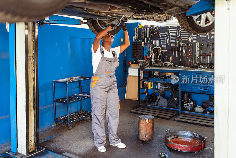 一名非洲妇女在汽车车间里做机械电子工程师，她正在修理一辆汽车