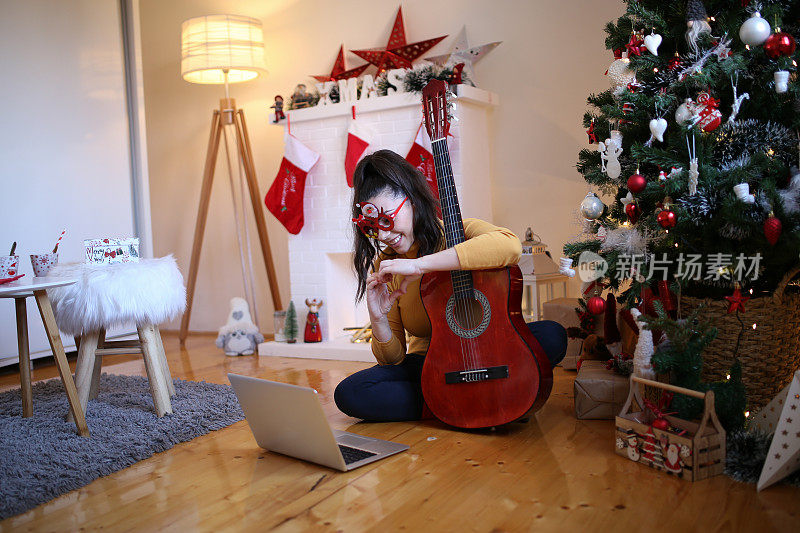 圣诞节假期，一个女人弹着吉他，享受着。库存图片