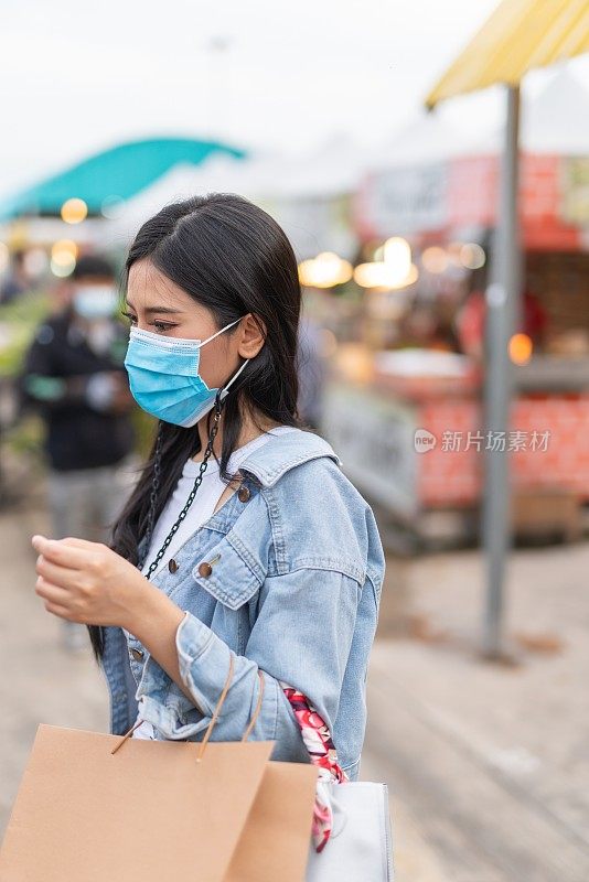 在泰国曼谷当地的夜市，一名戴着防护面膜的女性独自购物