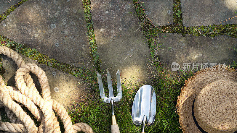 园艺设备。用铲子或铲子、园叉、草帽和绳子在花园里的石径上。农场的背景。前视图。年代
