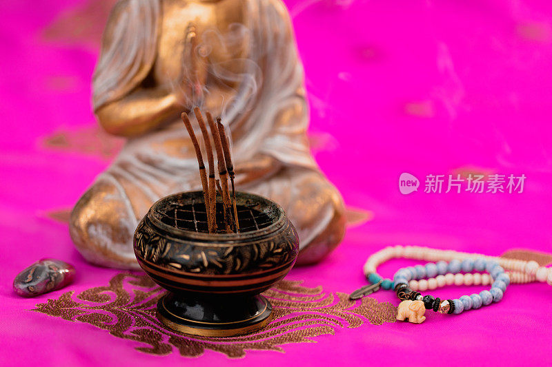在金佛和粉色印度教纱丽绳前的香碗中冒烟的香烛的特写