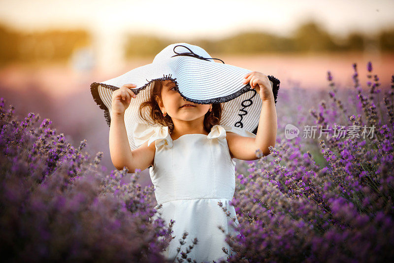 穿着白色连衣裙，戴着白色大帽子的小女孩在薰衣草地里。