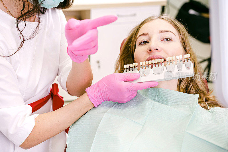 一位女士，穿着制服，戴着粉红色手套的口腔医生，在口腔处用阴影引导检查牙冠的贴面。