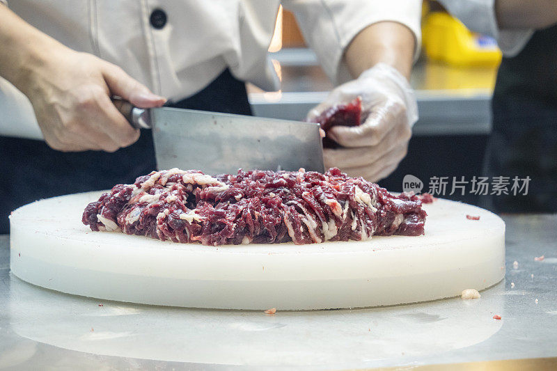 厨师在一家牛肉火锅餐厅的开放式厨房里用刀切牛肉