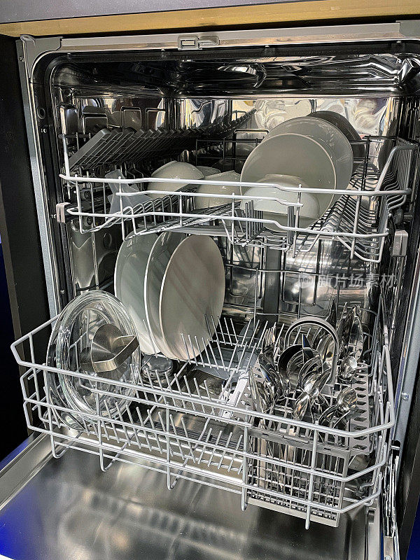 塑料洗碗机内部图像，餐具篮内盛有干净的不锈钢刀、叉及匙，半机器内放置清洗及干燥后可收纳的干净器具，白色餐盘、碗及玻璃炖锅盖