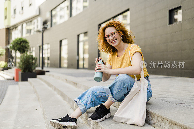 红发妇女用可重复使用的水瓶喝水，用可重复使用的棉生态生产袋购物。零废物生活方式概念