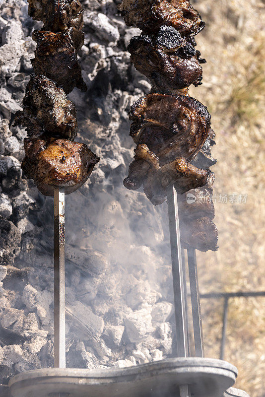 从上方看，装着羊肉的烤串在布满灰烬的炭火上烤着，缕缕炊烟朝镜头飘来