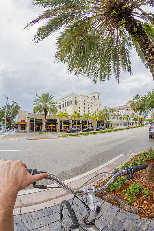 POV视角拍摄的年轻男子骑自行车在珊瑚山墙地区，迈阿密海滩，迈阿密，南佛罗里达州，美国。从个人角度拍摄异国情调的热带海滩旅游假期。