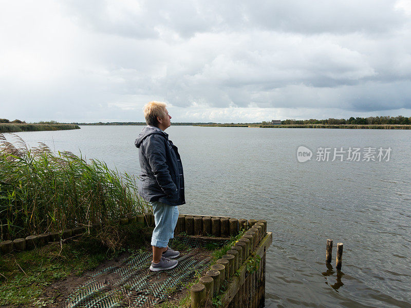 女人站在诺福克的宽宽的放松和享受宁静的景色在一个夏天的一天的水。