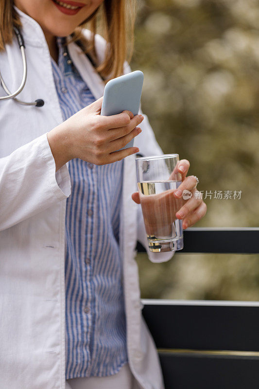 年轻的女医生站在阳台上，休息一下，用智能手机