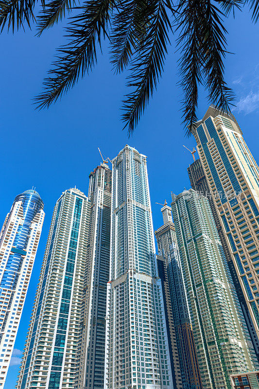 阿拉伯联合酋长国迪拜——高高的海滨摩天大楼聚集在一起，映衬着蔚蓝的午后天空。