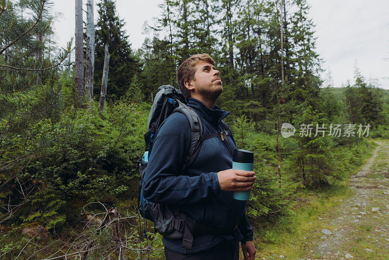 侧视图的男子背着背包徒步旅行在挪威的森林