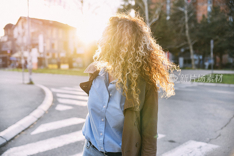 年轻的女士穿着时髦的衣服走在城市的街道上，环顾四周