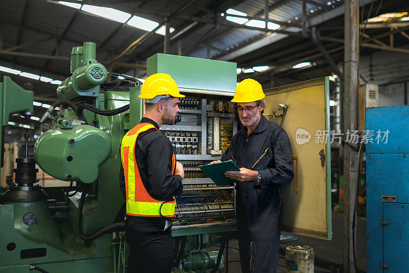 技术人员检查工业工厂生产机械控制柜的运行情况。技术员教新来的技工检查机械控制柜的操作。