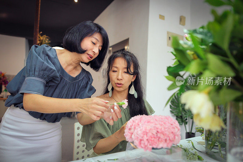 一位亚洲美丽的花艺女老师目前正在教花艺学生如何安排花艺材料，创造美丽的花艺作品。