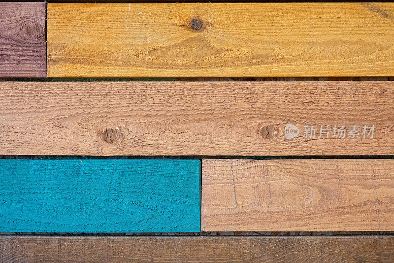 由未经处理的彩色粗糙木板制成的墙壁碎片。蓝色、黄色和天然木色。背景。纹理。的形式。