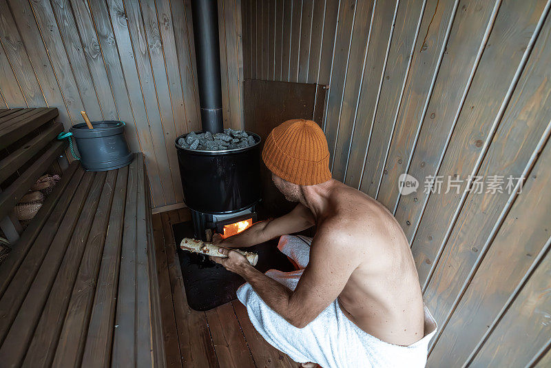 一个年轻人在一个漂浮的桑拿浴室里放松，他打开了烧木头的炉子