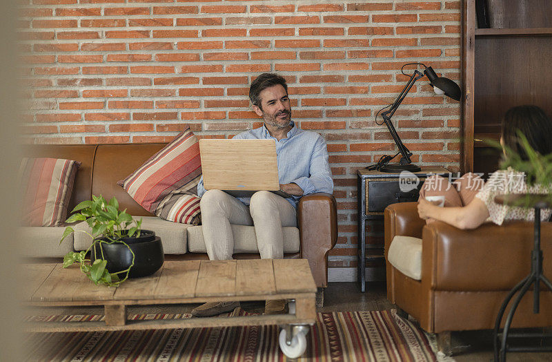 一对成熟的夫妇一边在公寓的客厅聊天，一边用笔记本电脑在网上购物