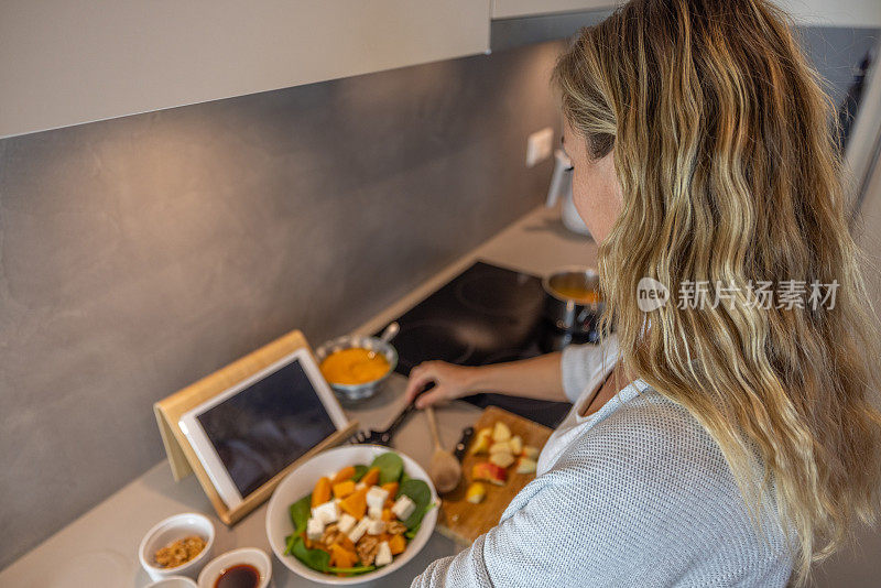 妇女在家里按照数字平板电脑上的食谱准备健康食品