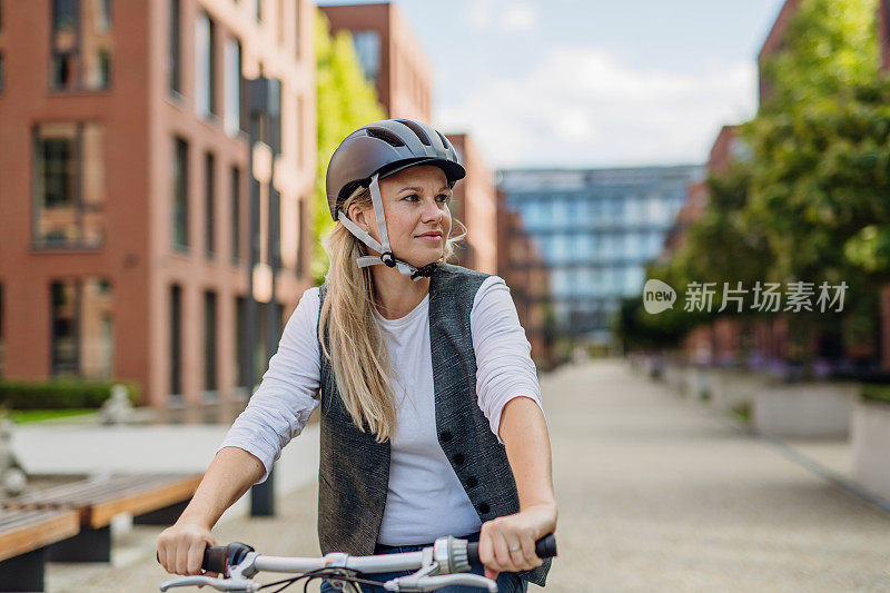 漂亮的中年妇女骑着自行车穿梭于城市之间。女性在漫长的工作日后骑自行车下班。