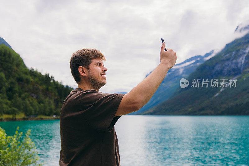 男旅行者在山湖边拍摄田园诗般的自然风光