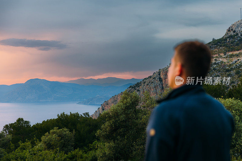 男子欣赏神奇的日落俯瞰大海和山脉