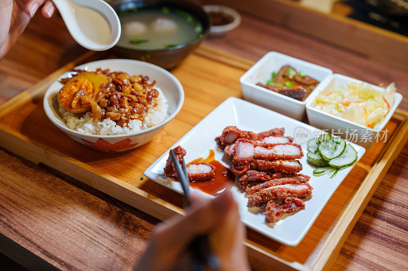 一个年轻人正在享用台湾式便当，这是一种由红烧肉饭、汤和配菜组成的盒饭。