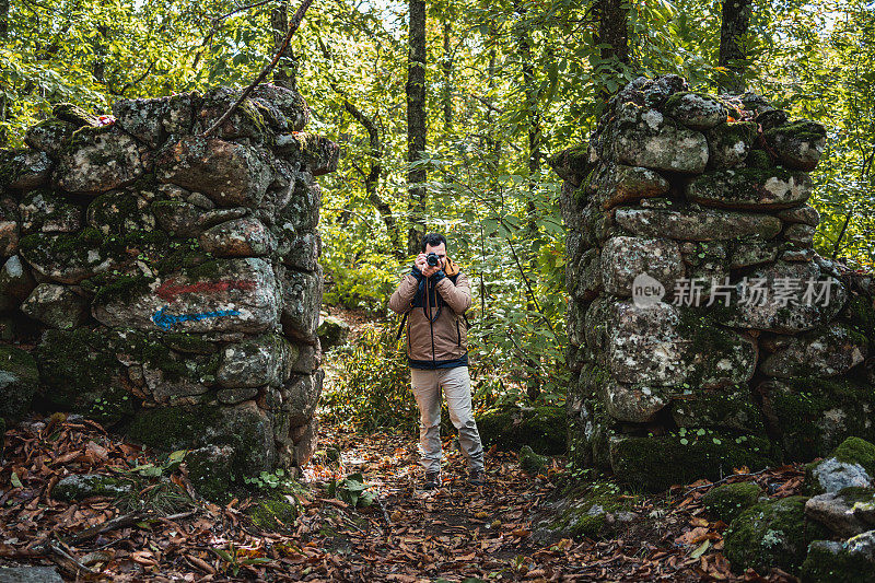年轻美丽的摄影师在森林里的老石门上拍照，看着相机
