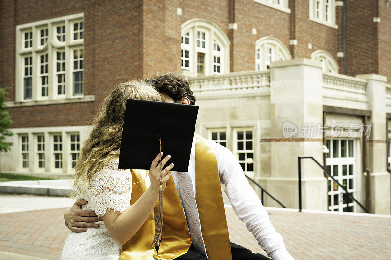 美国印第安纳州一座砖砌建筑外，男毕业生和女毕业生在毕业礼帽后接吻