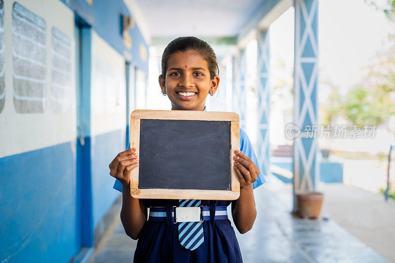 微笑的女孩孩子在学校走廊的广告，教育和学习公告拿着空板看着镜头。