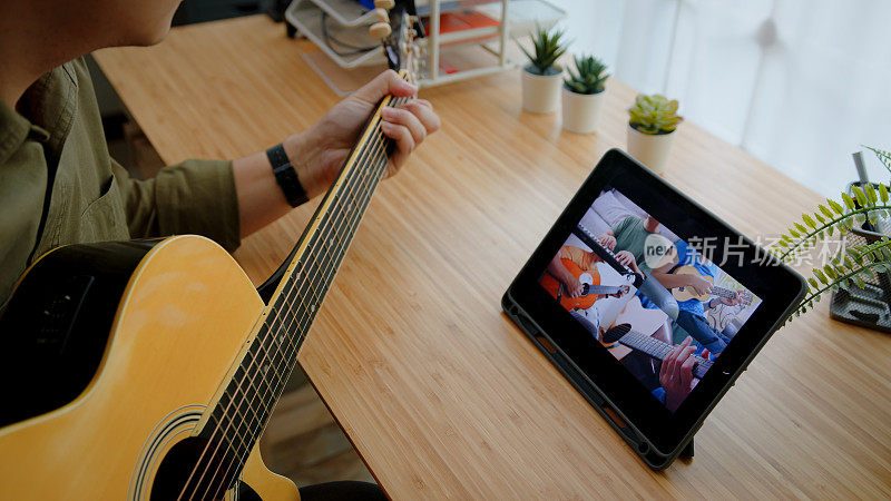 近距离的人的手演奏原声吉他与乐队通过视频会议音乐应用程序，而呆在家里。