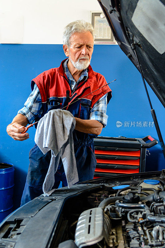 一位汽车修理工正在修车车间修理汽车并检查机油。