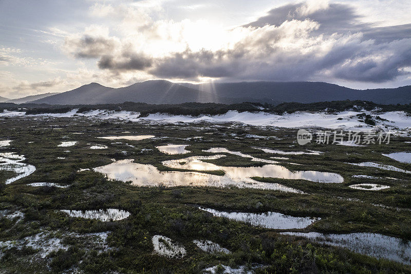 地区沙丘和湖泊的背景山在阳光下云层之间。