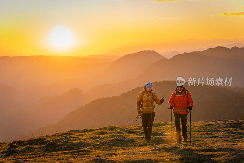 徒步者在草地上爬山，浪漫多彩的日落