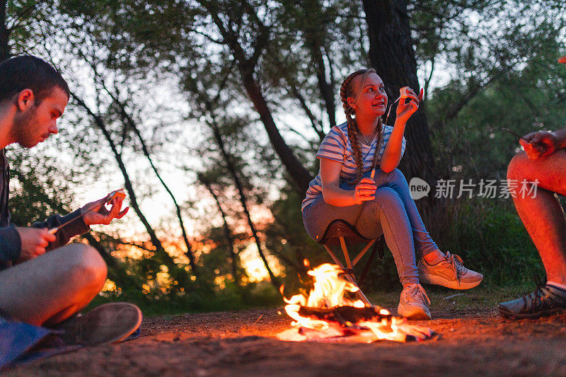黄昏时分，年轻女子在篝火上烤棉花糖，与朋友在户外露营