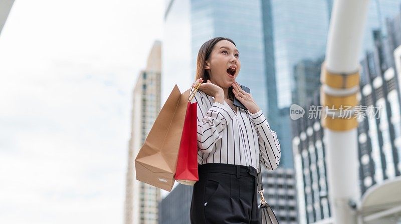 迷人聪明的亚洲女商人雇员在曼谷市中心商业区疯狂购物后，看到另一个狂欢节销售，她笑得很开心