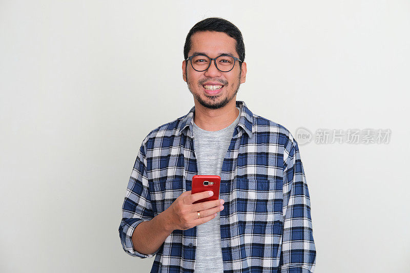 成年亚洲男子拿着手机对着镜头微笑