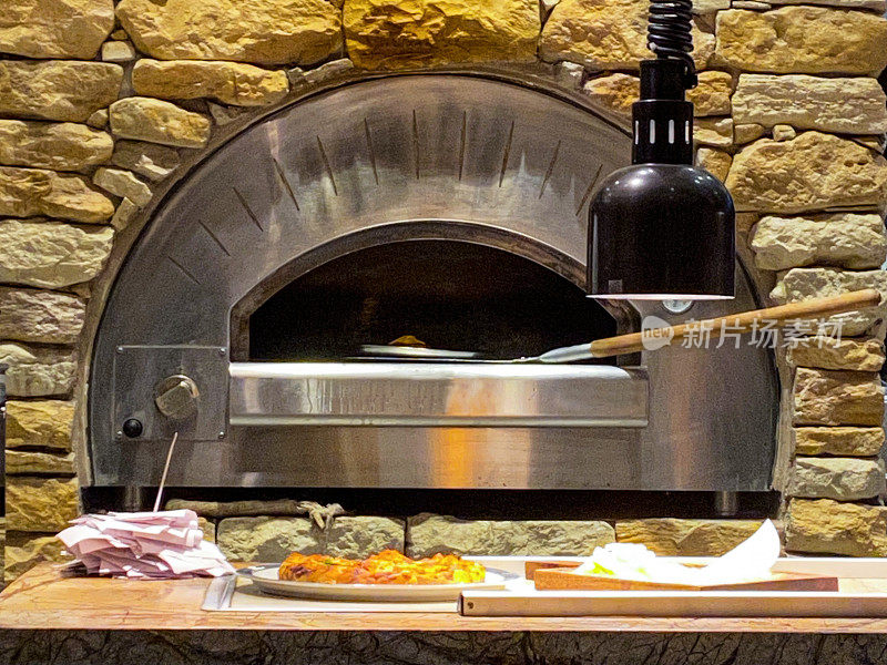 近距离图像燃气披萨烤箱镶嵌在砖墙与金属披萨桨，意大利餐厅披萨炉，打开烤箱门，关注前景