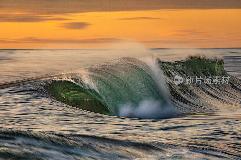 平滑的海浪打破清晨金色的光和戏剧性的天空日出