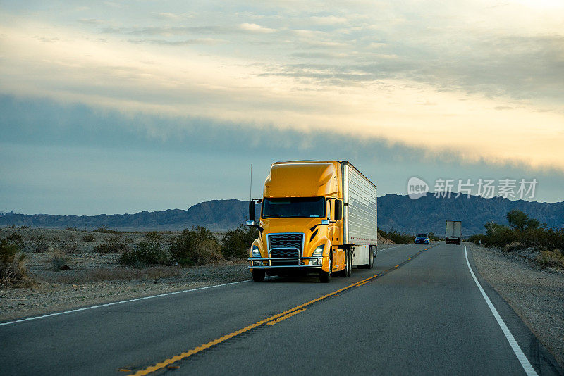一辆黄色的半挂式卡车行驶在双车道公路上，日落时分美丽的云雾缭绕