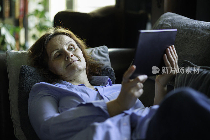 一个女人躺在家里的沙发上用平板电脑